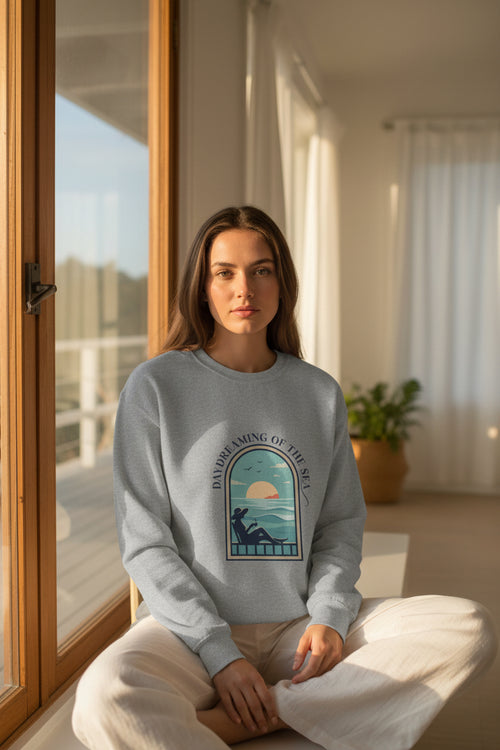 Gray sweatshirt with a graphic design of a person by the sea and 'Daydreaming of the Sea' text on a white background.
