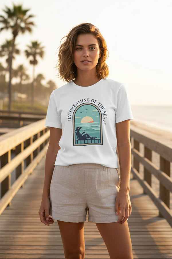 White t-shirt with a graphic design of a woman on a beach and text 'Daydreaming of the Sea' on a white background.