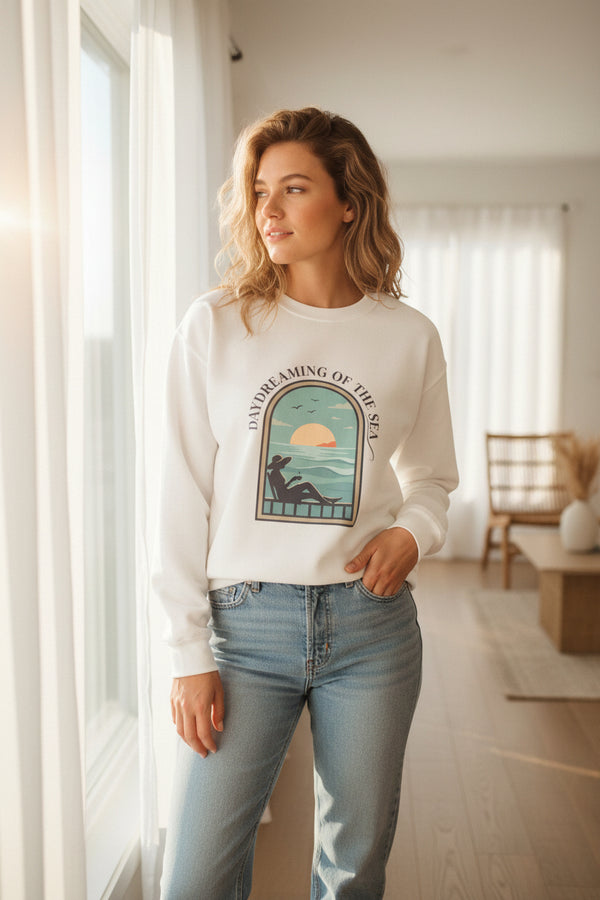 White sweatshirt with a graphic design of a person by the sea and 'Daydreaming of the Sea' text on a white background.