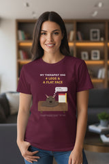 Maroon t-shirt with a graphic of a dog on a couch and text about a therapist, on a white background.
